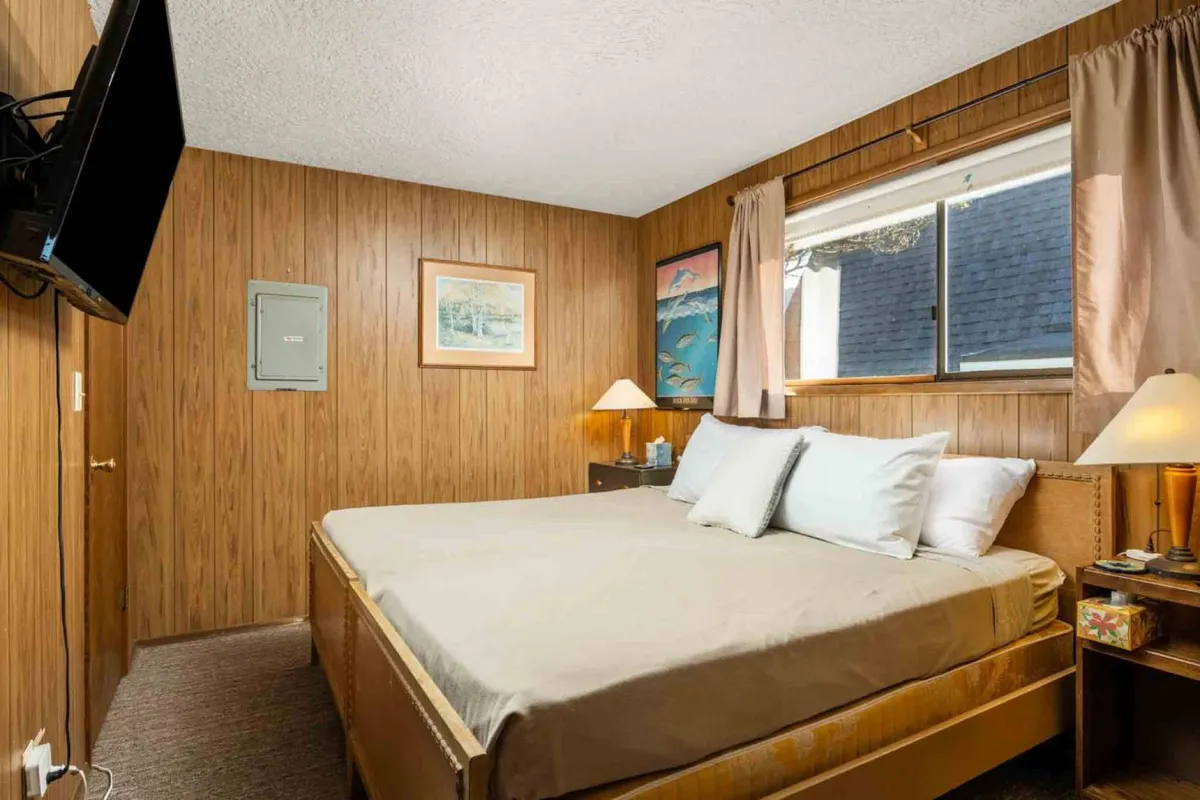 A sunlit bedroom with a comfortable bed set against a window that fills the room with natural light. Thoughtful touches like a stylish lamp, wall art, and a cozy reading nook create an inviting space designed for relaxation or unwinding with a late-night movie.