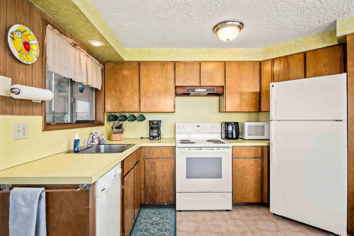 The kitchen is shown with warm wooden cabinets, white appliances, and cheerful yellow countertops. The layout feels spacious and inviting, ideal for preparing family-style meals or casual snacks. It conveys a sense of homey comfort and practicality, emphasizing the kitchen’s role as a center for activity and connection.