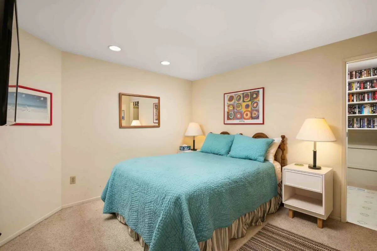 A cheerful bedroom featuring a bed with a turquoise cover, soft lighting from bedside lamps, elegant framed artwork, and a mirror that reflects the room’s warm ambiance. The space feels both inviting and thoughtfully appointed for restful sleep.
