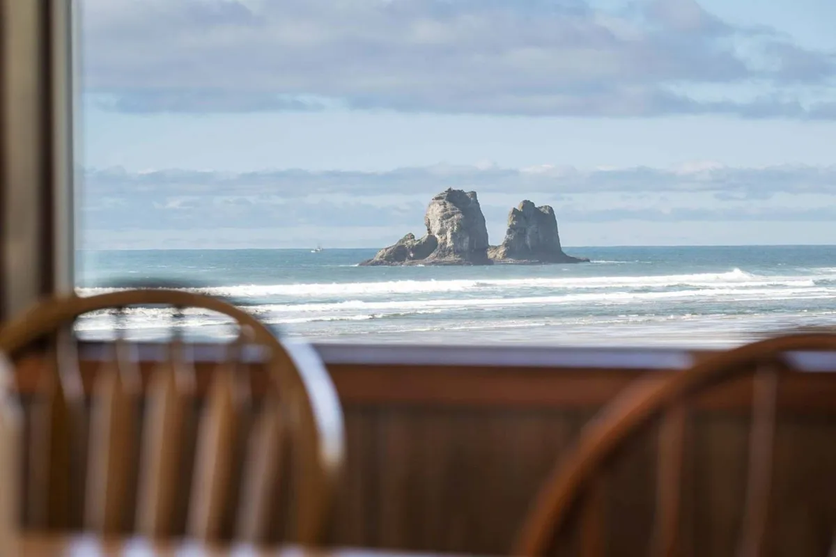 This image presents a breathtaking view of the ocean with dramatic rock formations and undulating waves beneath a clear blue sky. The vantage point suggests this is the sort of scenery visible from the communal spaces inside, reinforcing the promise of unobstructed Pacific views and the natural beauty that’s ever-present through the home’s panoramic windows.